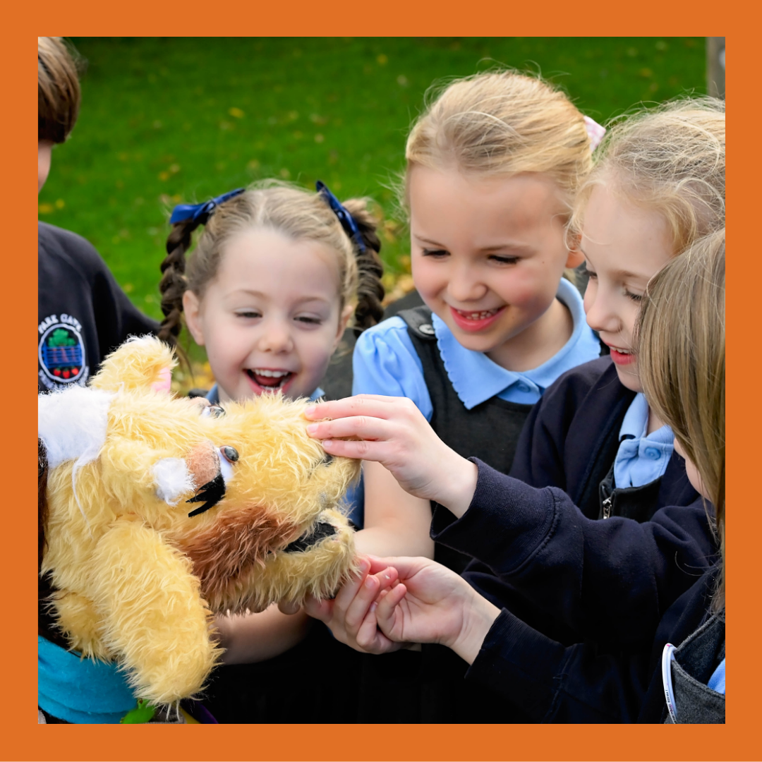 School children smiling whilst touching Harold the giraffe